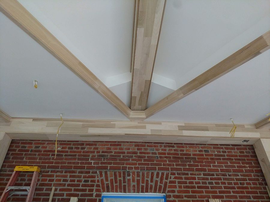 Ceiling with wood beams, brick wall below, and a ladder.