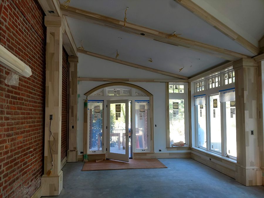 Interior of a room under construction with brick wall, windows, and light wooden beams.