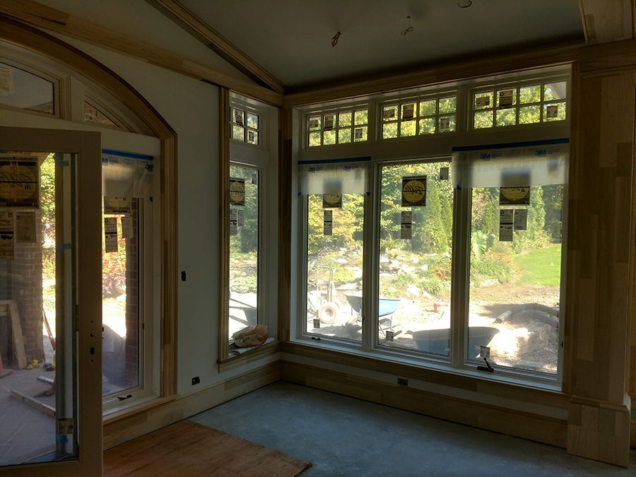 Interior of a room with large windows, unfinished, looking out to greenery, wood trim.