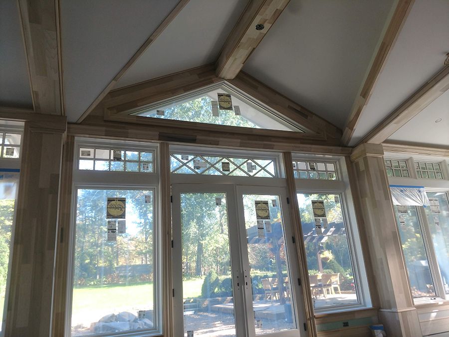 Interior view of a sunroom under construction with large windows and wooden beams.