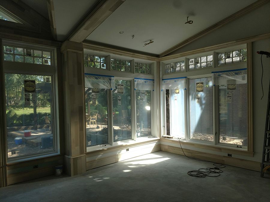 Sunlit room with large windows, unfinished construction, visible beams, and plastic covering windows.