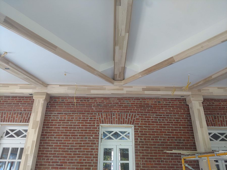 Brick wall with wooden beams forming a ceiling; white windows, unfinished construction.