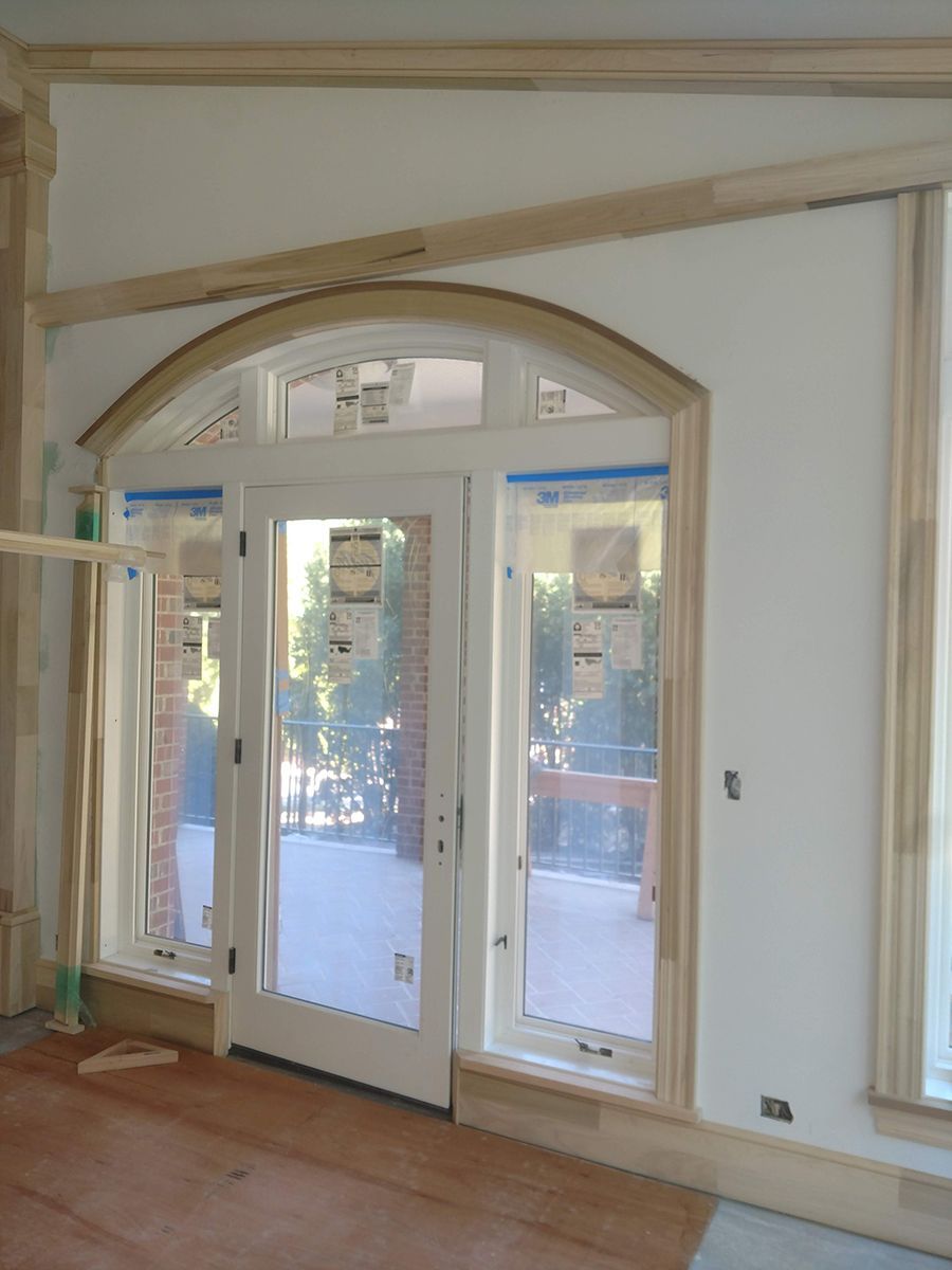 Interior view of door and window with wooden trim, unfinished construction, white wall.