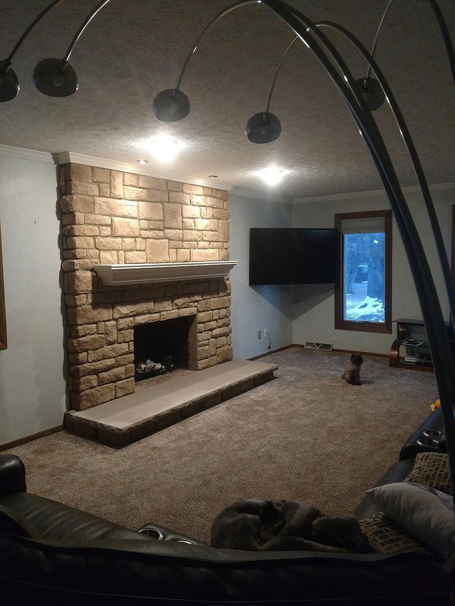 Living room with stone fireplace, TV, brown carpet, and an arching floor lamp.