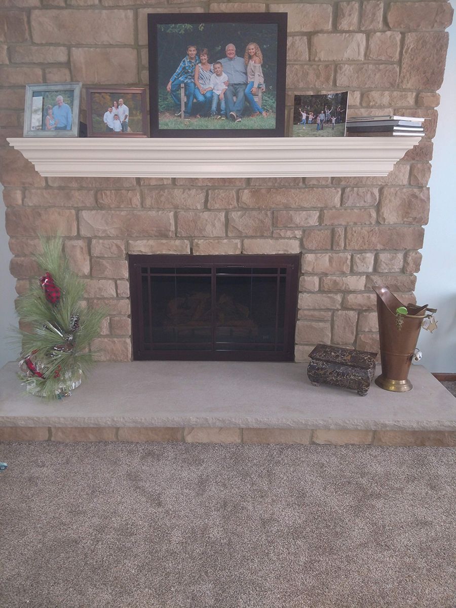 Fireplace with stone facade, wooden mantel holding framed photos. Christmas decor on hearth.