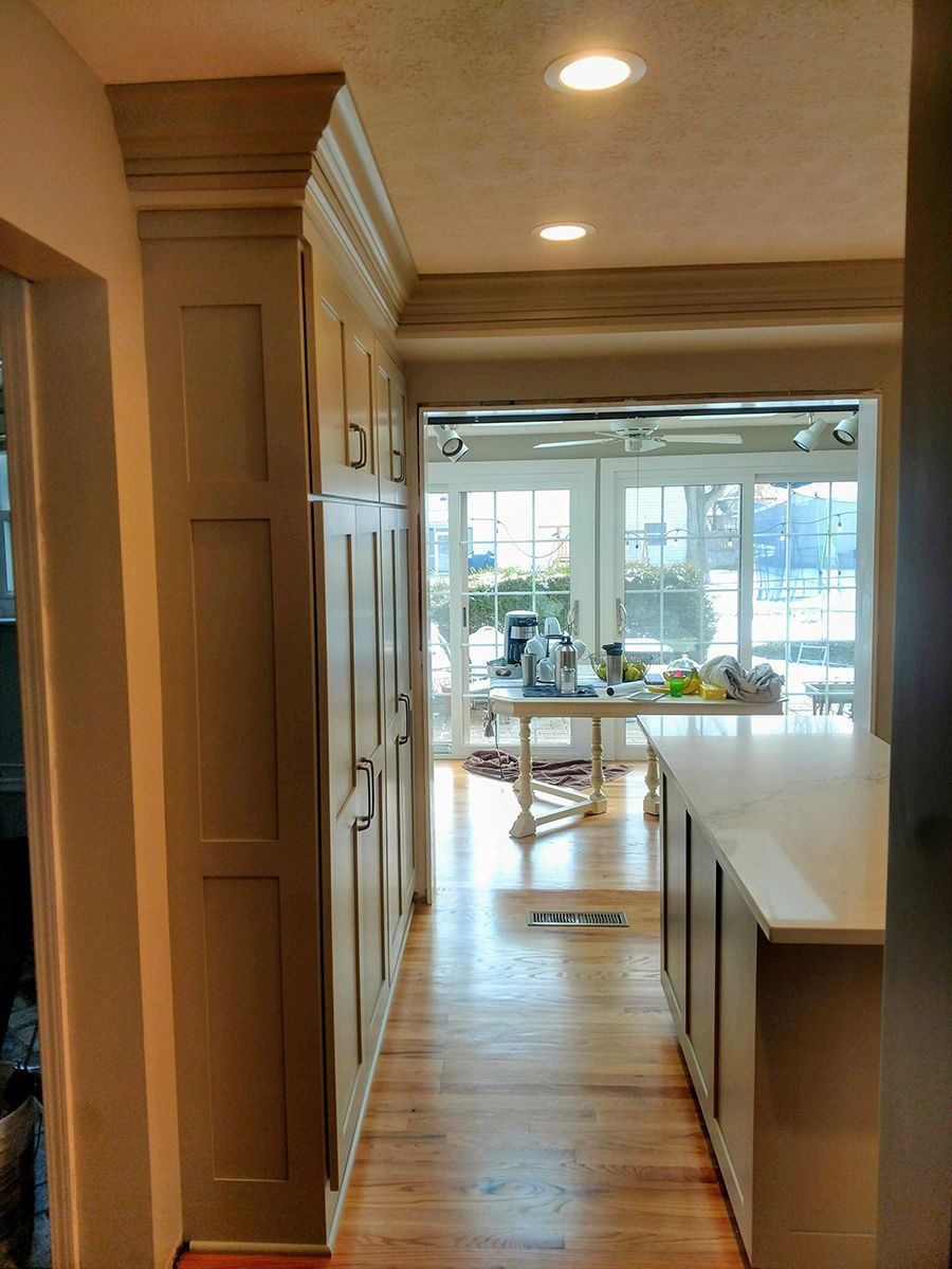 Kitchen with light-colored cabinets, wood floor, and counter overlooking a bright view through glass doors.