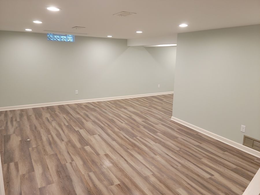 Empty finished basement with light wood-look flooring, light green walls, and recessed ceiling lights.