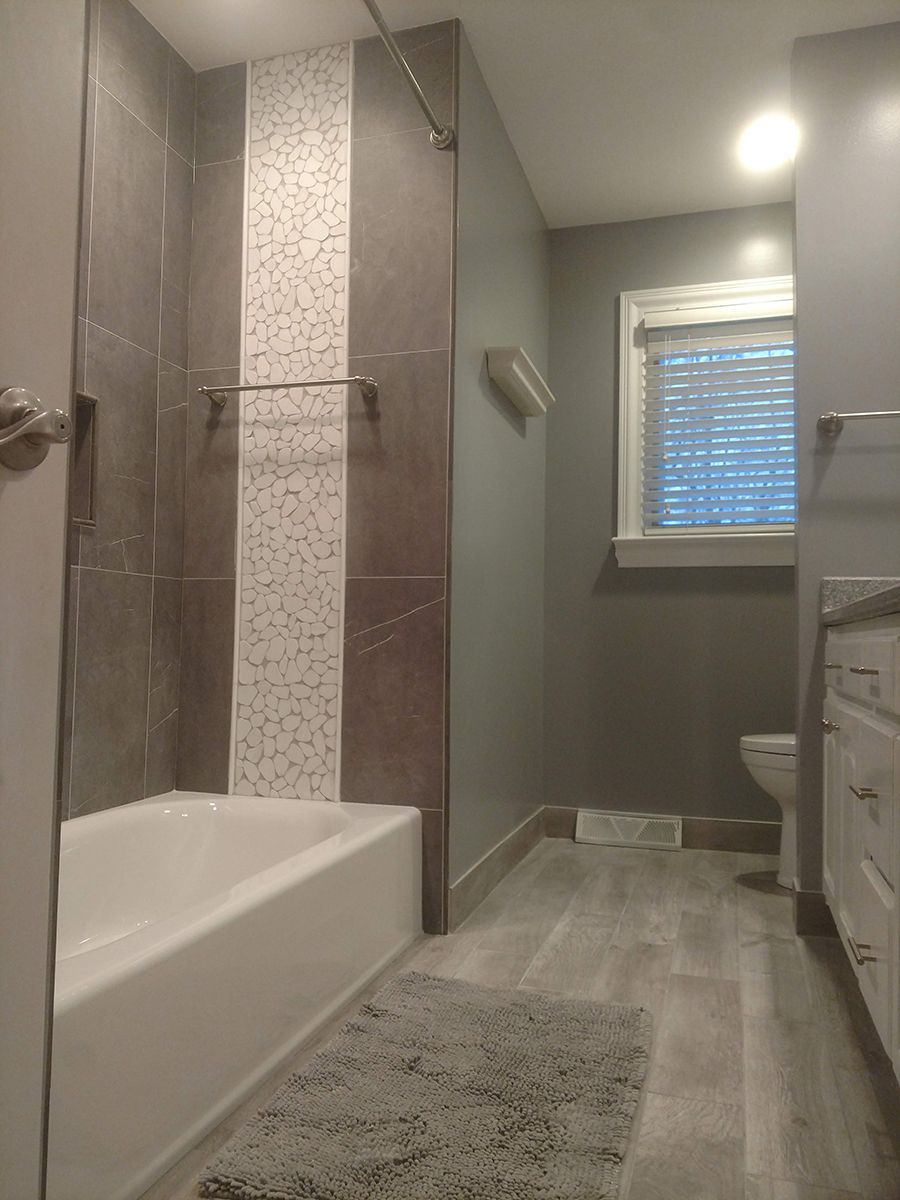 Bathroom with gray tile, shower with decorative strip, bathtub, and window.