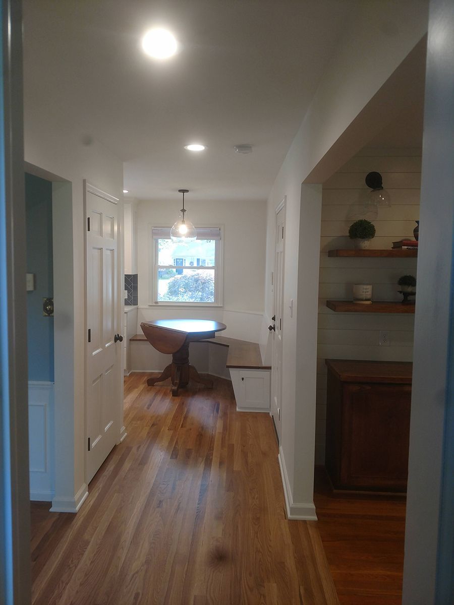 Hallway with hardwood floor, leading to a dining area with a round table and built-in bench. White walls and trim.