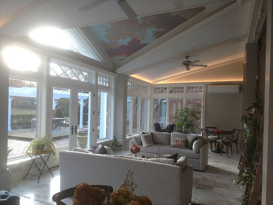 Sunroom interior with sofas, marble floors, large windows overlooking a patio, and a painted ceiling.