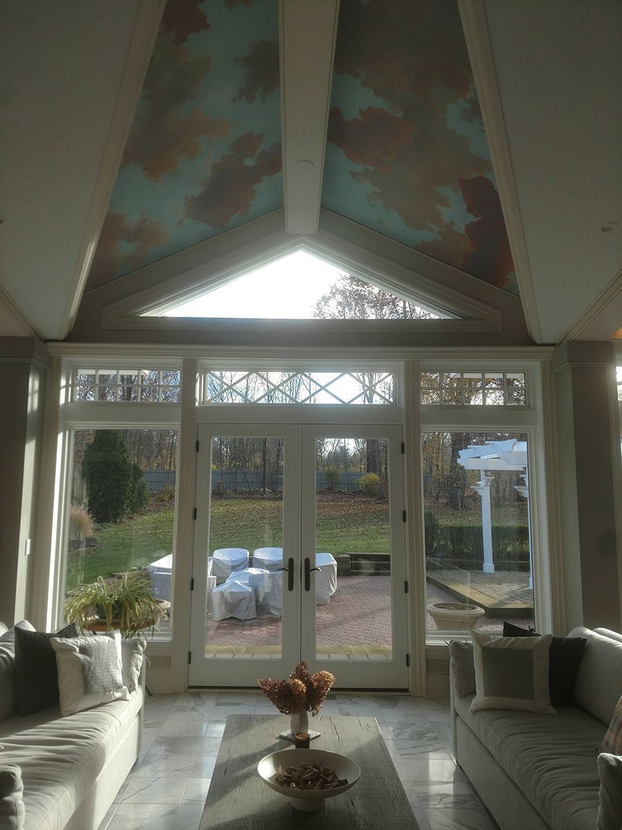 Sunroom with painted ceiling, glass doors to the outside, and white couches.