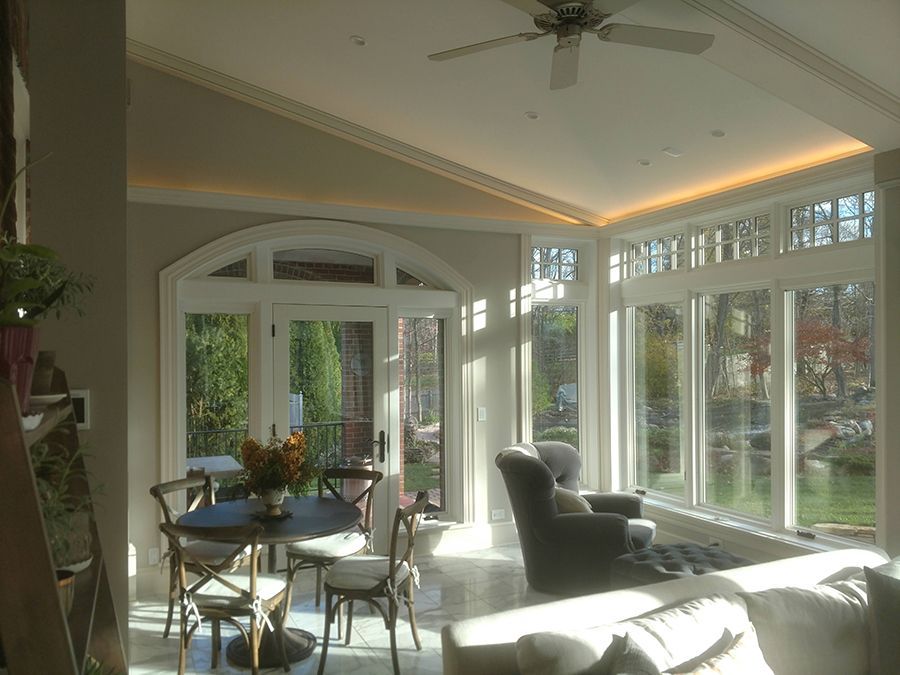 Sunroom with windows and arched doors, showing a table, chairs, and armchair, bathed in sunlight.