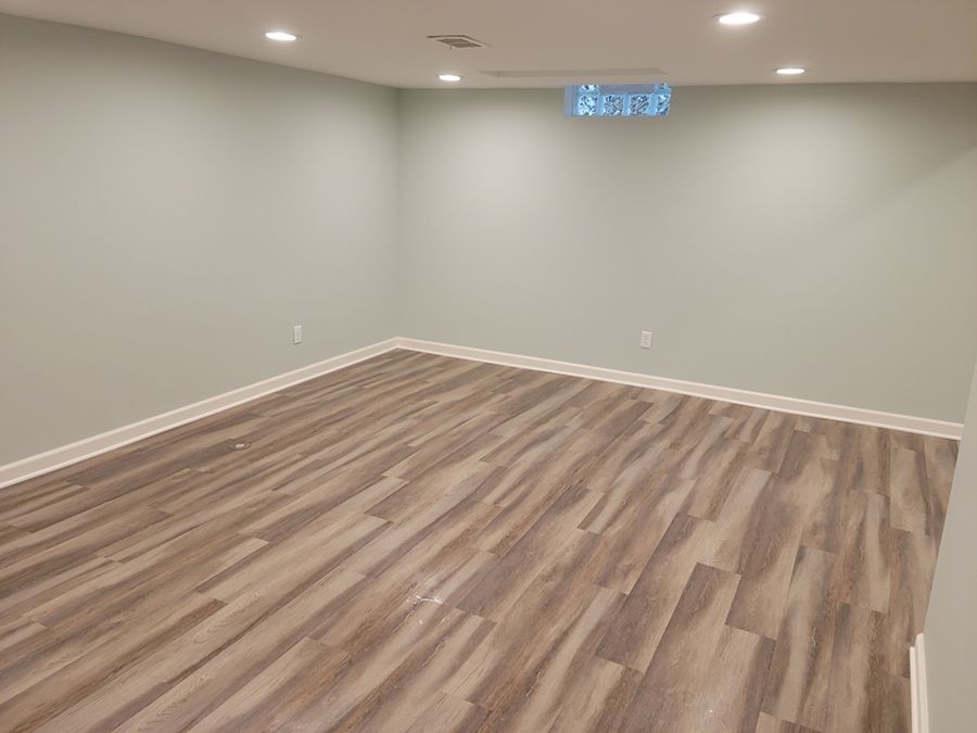 Empty room with light wood-look flooring and pale green walls, lit by recessed ceiling lights.