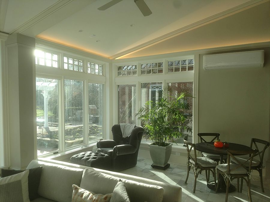 Sunroom with large windows, lounge chair, dining table, and large potted plant.