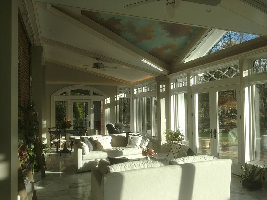 Sunroom with white sofas, large windows, and a painted ceiling of clouds.
