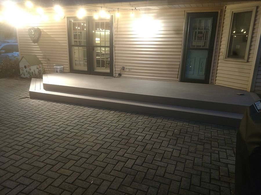 Backyard patio with steps leading to two doors and a blue door. Overhead lights and brick pavers.