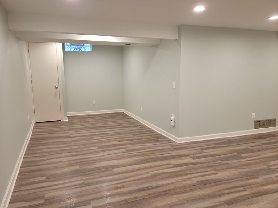 Empty finished basement with light gray walls, wood-look flooring, and white trim.