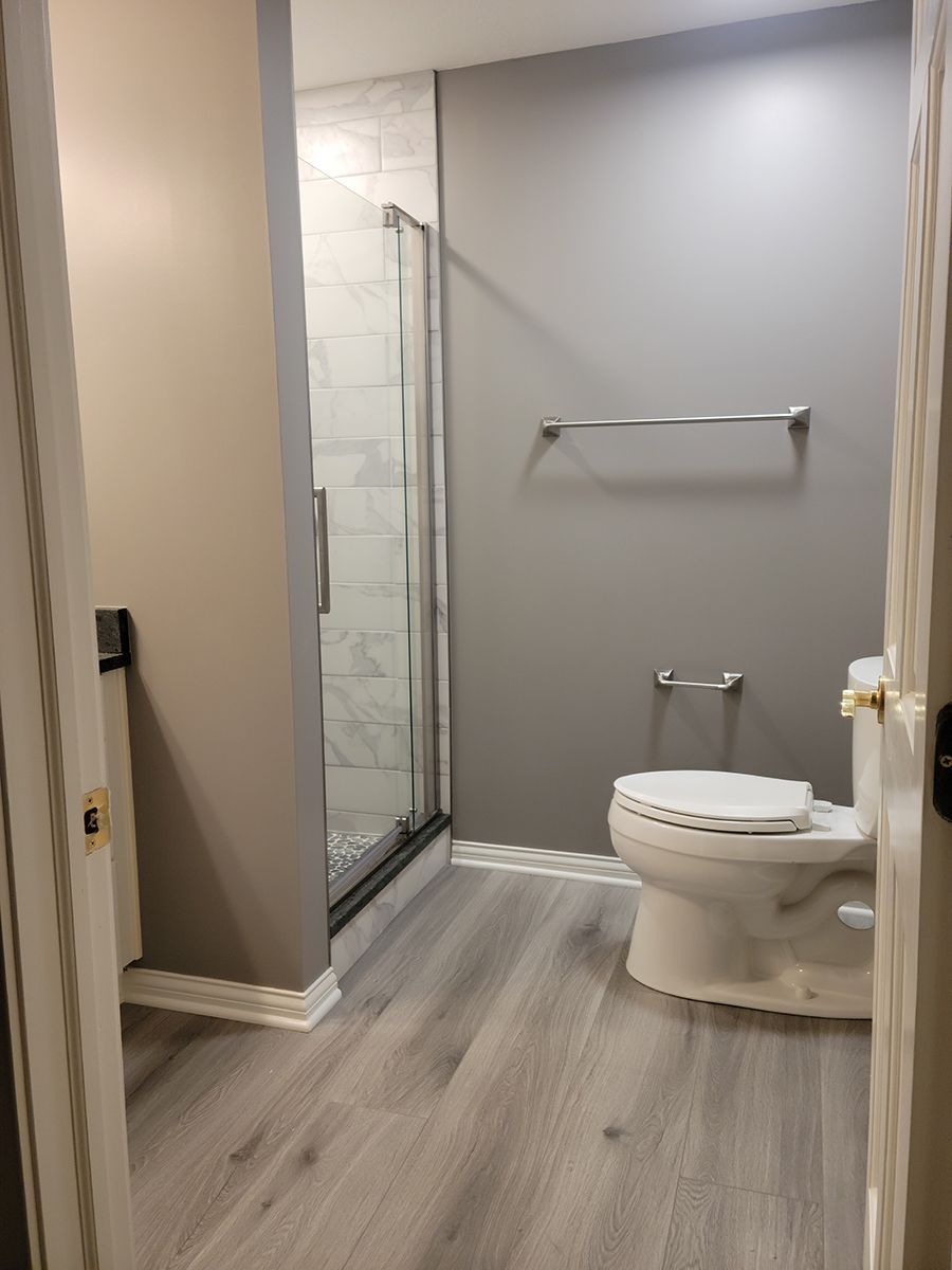 Bathroom with gray and beige walls, a glass shower, toilet, and silver towel rack.