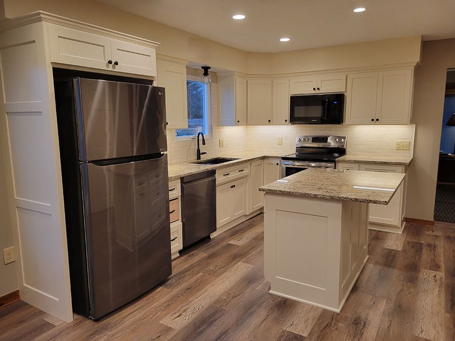White kitchen with stainless steel appliances, granite countertops, and wood-look flooring.