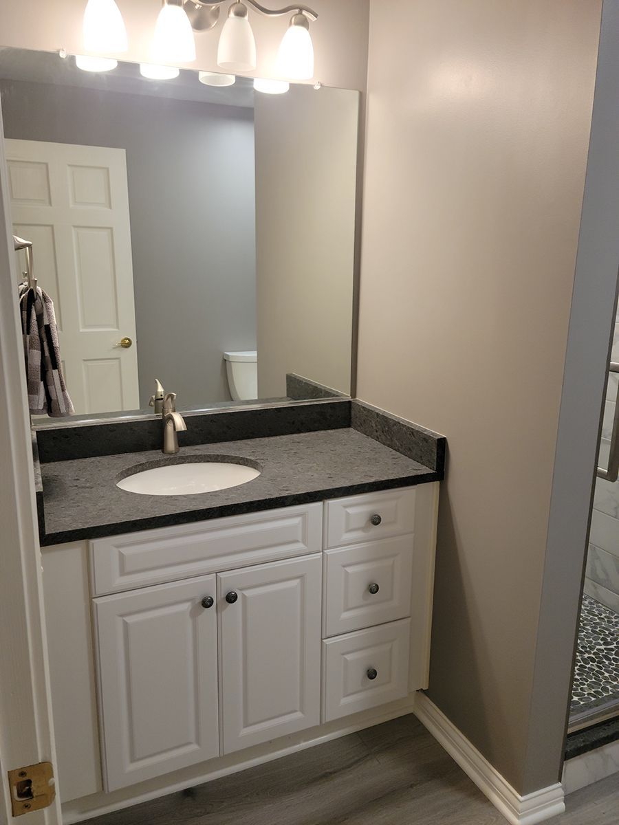 White bathroom vanity with dark countertop, sink, and mirror. White door and light gray walls.