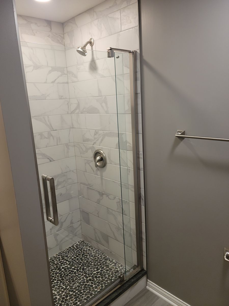 Shower with marble-look tile, pebble floor, glass door, and silver fixtures; gray walls.