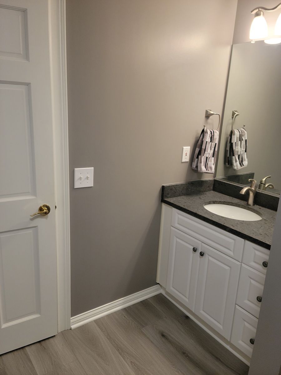 Bathroom with white vanity, gray countertop, and light gray walls. Door on left, mirror above sink.