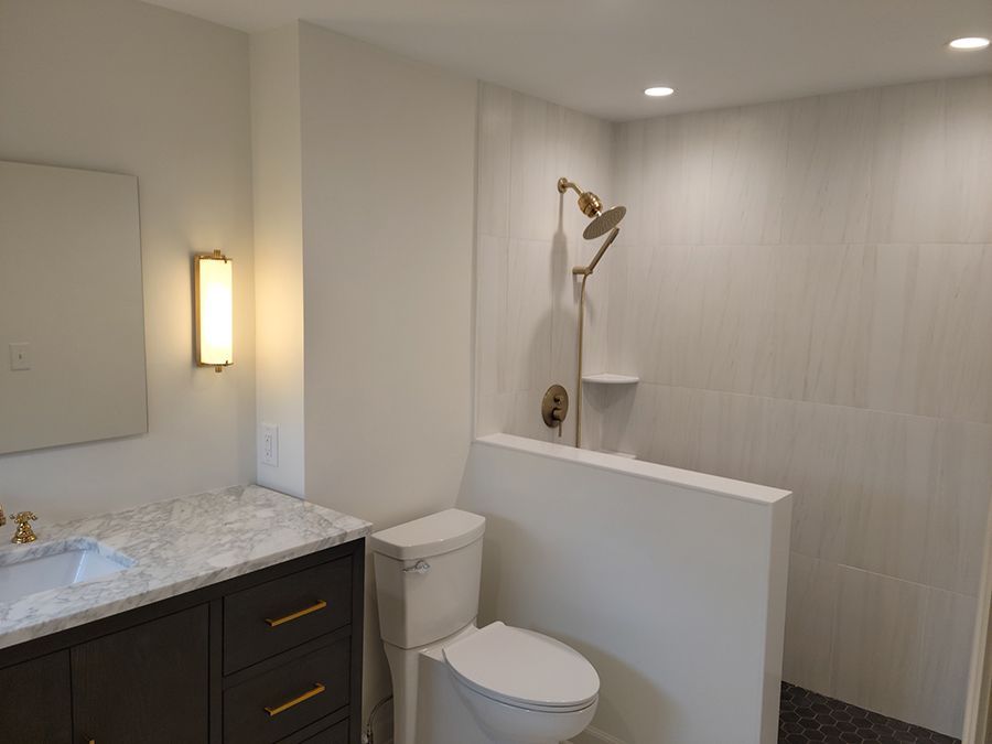 Modern bathroom with shower, toilet, and vanity; white and gold accents.