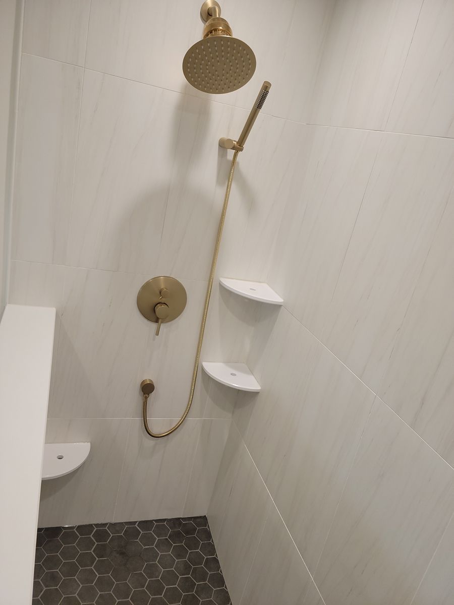Gold shower fixtures against white tile; gray hexagonal floor.