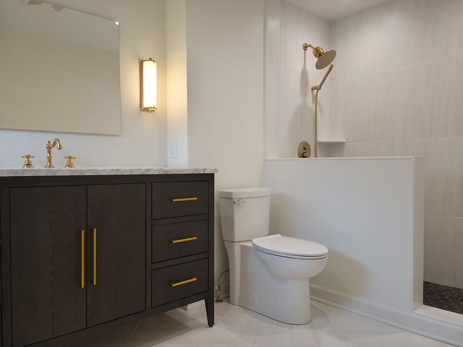 Bathroom with dark wood vanity, gold fixtures, white toilet, shower, and large mirror.