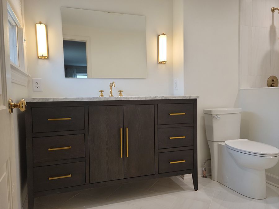 Modern bathroom with dark wood vanity, gold fixtures, and a white toilet.