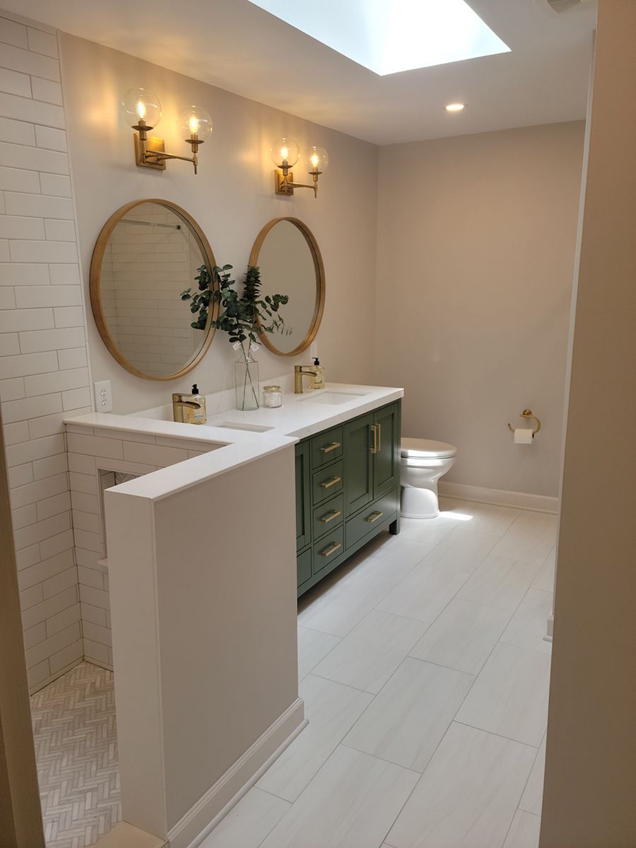 Bathroom with olive green vanity, white tile, two round mirrors, and skylight.