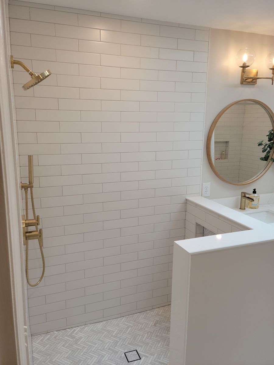 Bathroom with white tiled shower and gold fixtures, featuring a round mirror and countertop.