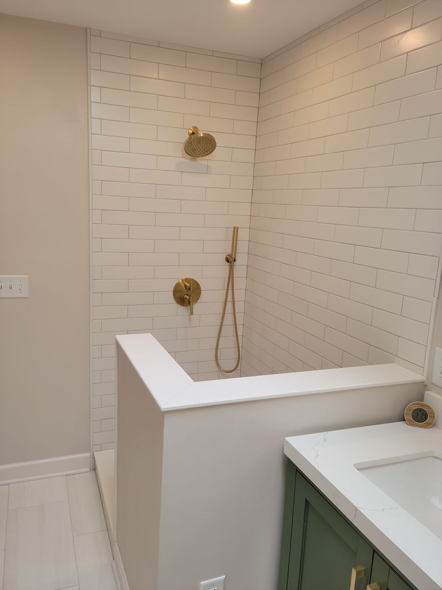 A modern bathroom with a white tiled shower area, gold fixtures, and a half-wall divider.