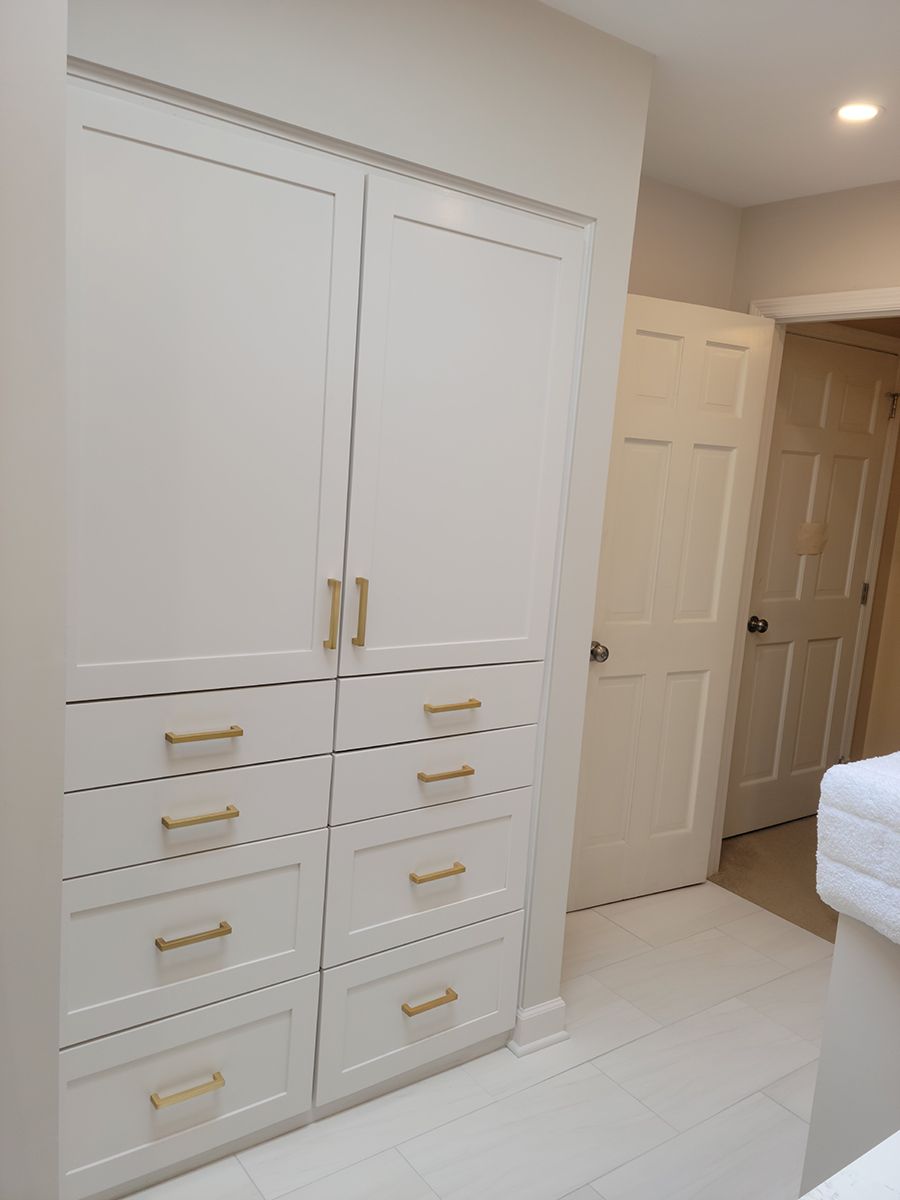 White closet with gold handles and drawers, next to a white door.