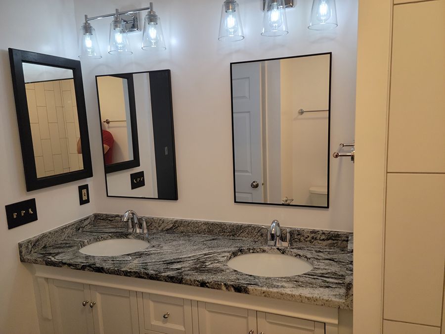 Bathroom with dual sinks, mirrors, and granite countertop. White cabinets and walls.