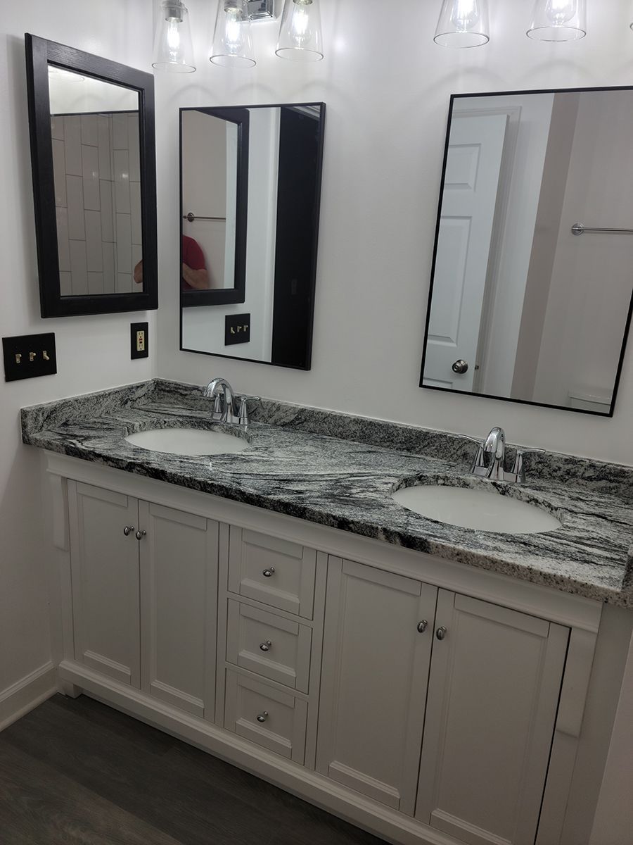 Bathroom with double vanity, granite countertop, two mirrors, white cabinets, and silver fixtures.
