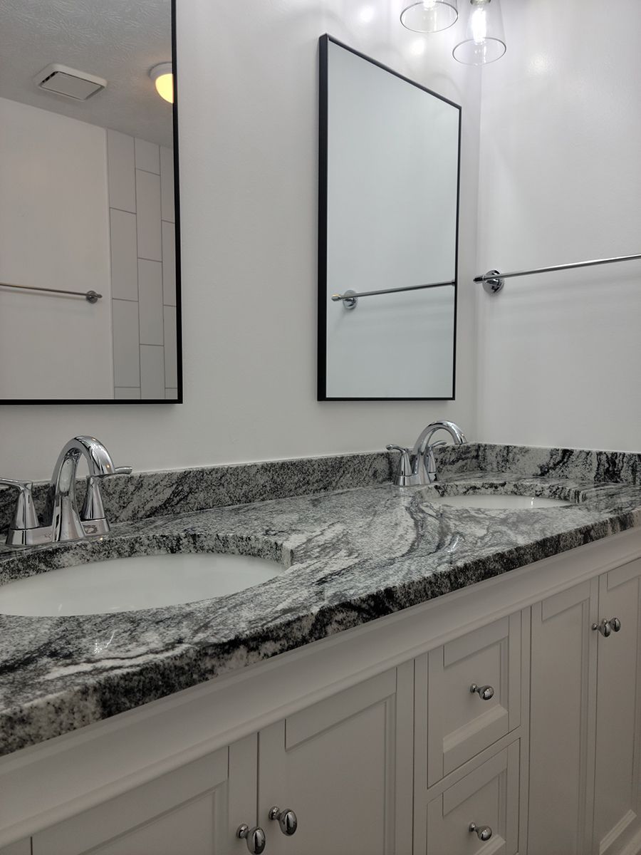 Bathroom vanity with two sinks, a granite countertop, white cabinets, and mirrors.