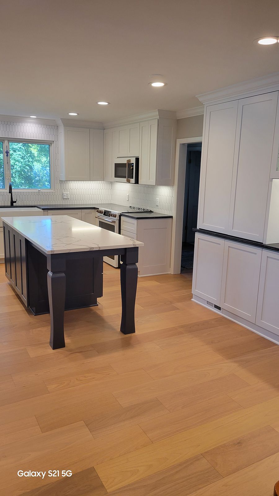 Spacious kitchen with wood floors, island, white cabinets, and a doorway.
