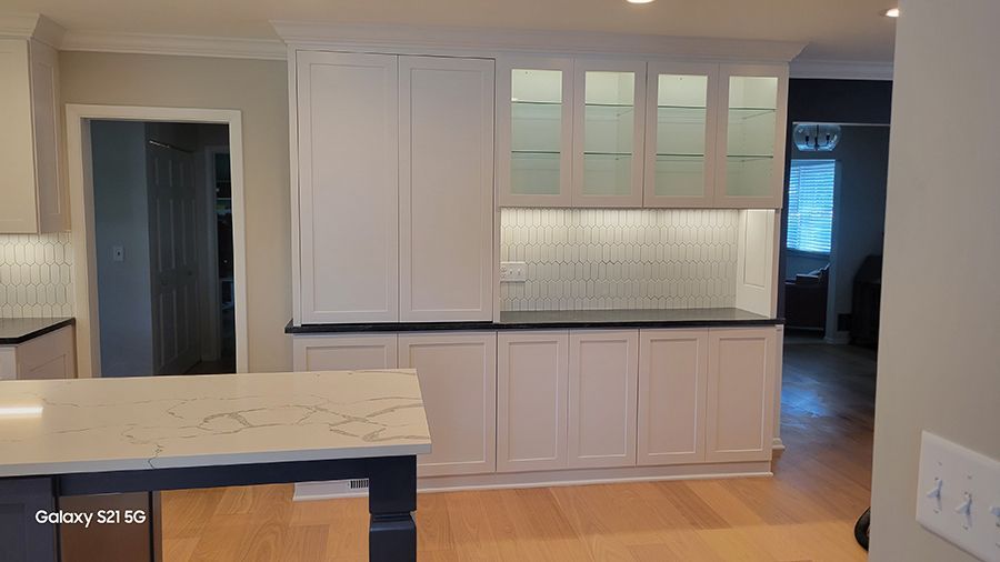 White kitchen cabinets with glass doors, black countertop, light backsplash, and wood floor.
