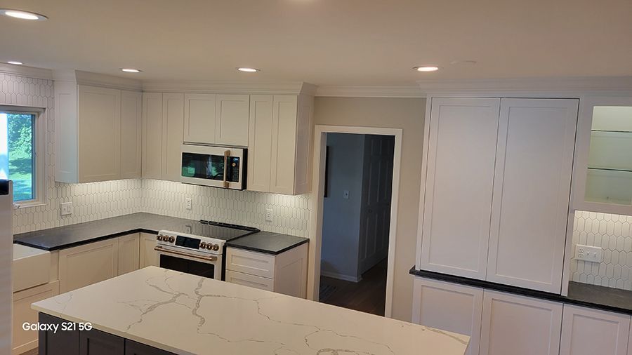 Modern kitchen with white cabinets, dark countertops, island, and stainless steel appliances.