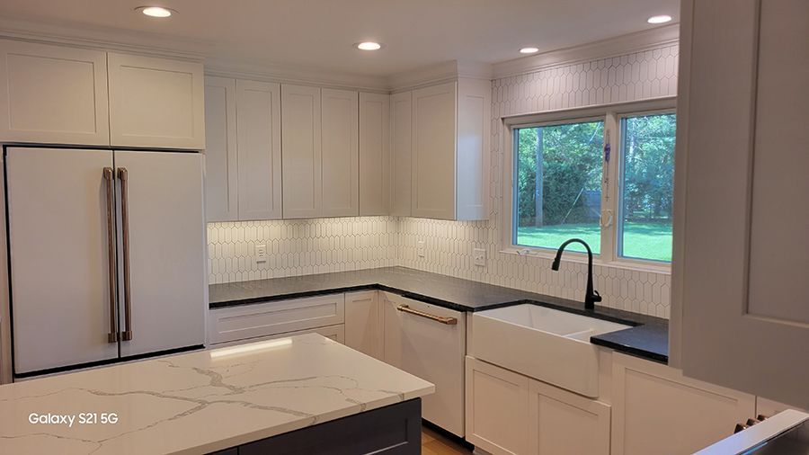 Modern white kitchen with island, black countertops, and stainless steel appliances.