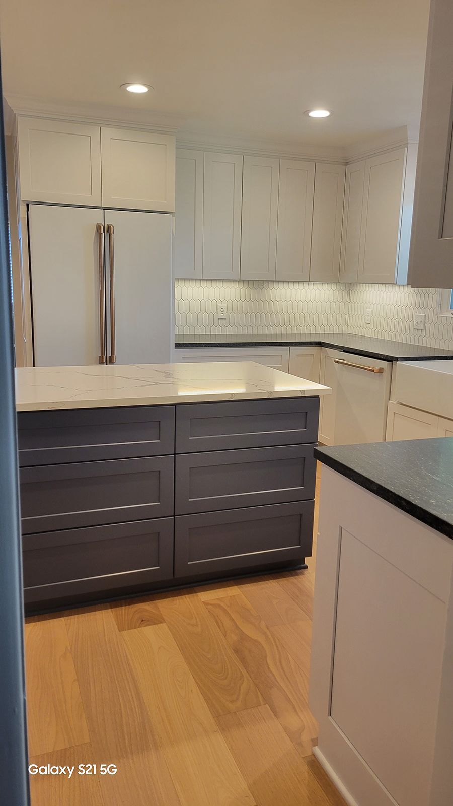 Modern kitchen with white and gray cabinets, island with a white countertop and dark gray base.