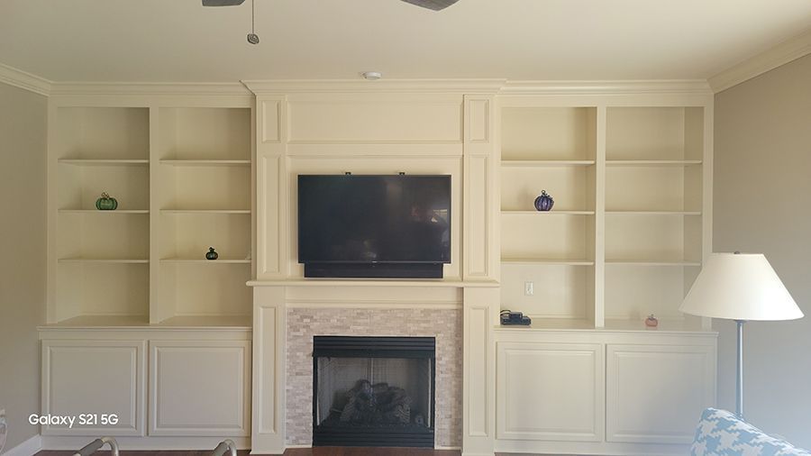 Built-in cream-colored shelves flank a fireplace with a mounted TV; a lamp is visible to the right.