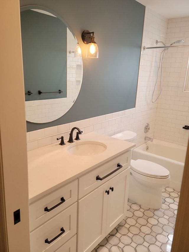 Modern bathroom with white vanity, toilet, and bathtub; gray accent wall, black fixtures, and patterned floor.