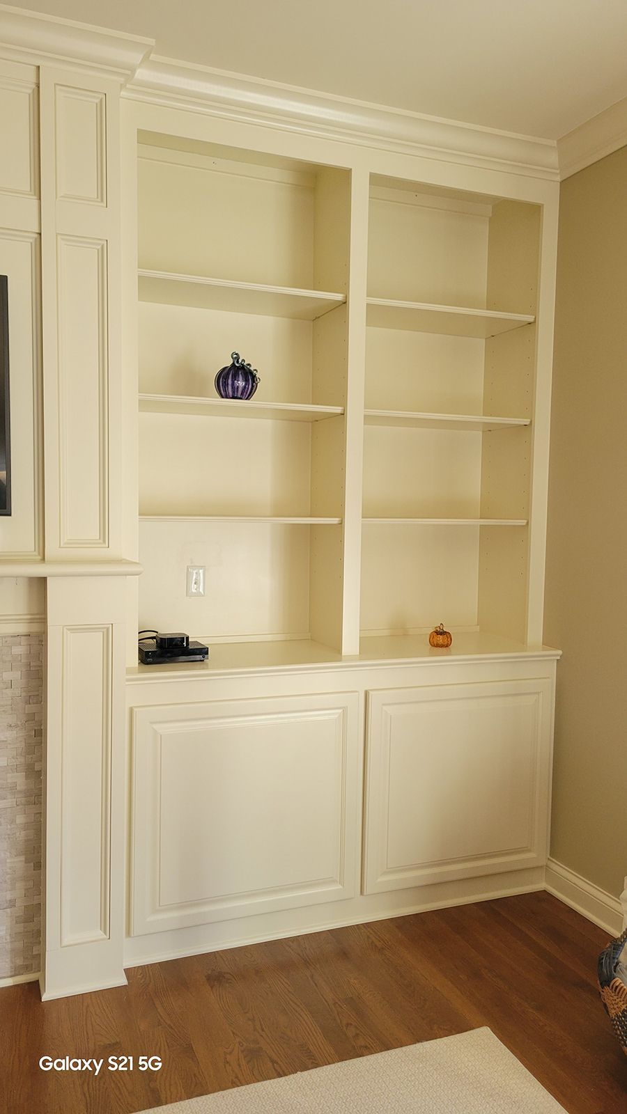 Built-in cream-colored bookcase with open shelves and cabinets, built into the wall.
