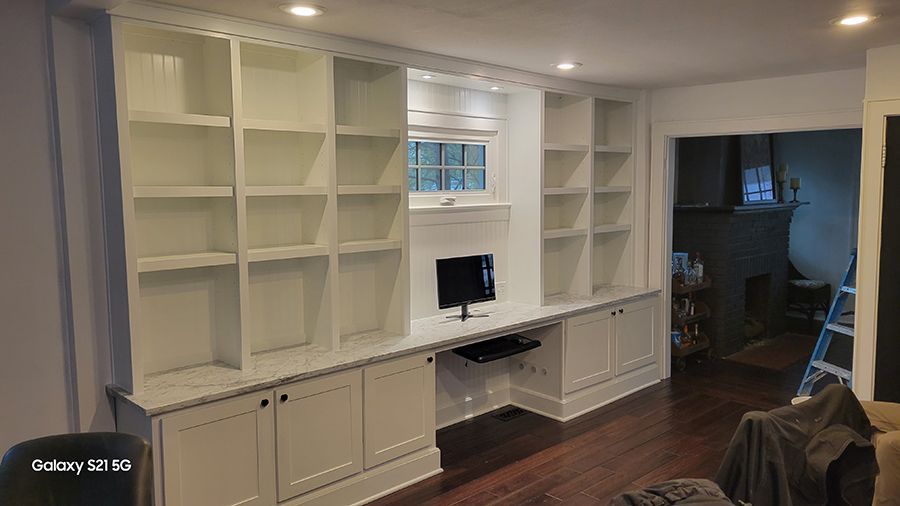Built-in white bookshelves with desk and cabinets. A small window sits above the computer.
