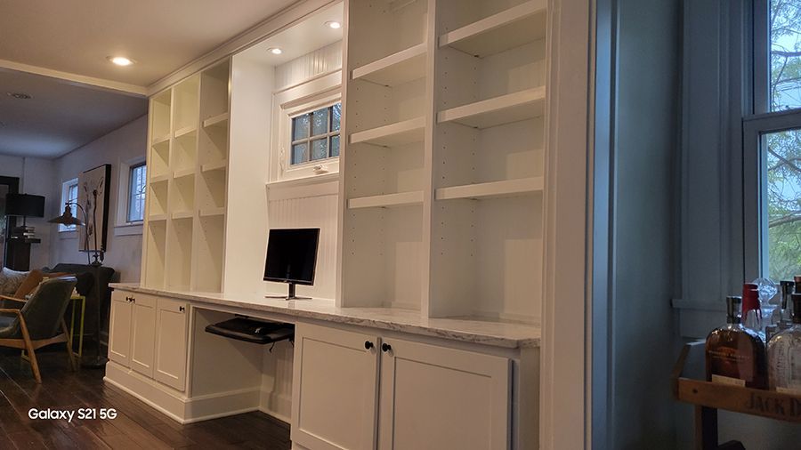 Built-in white bookshelves with a desk area, window, and cabinets. Interior room with wood floor.
