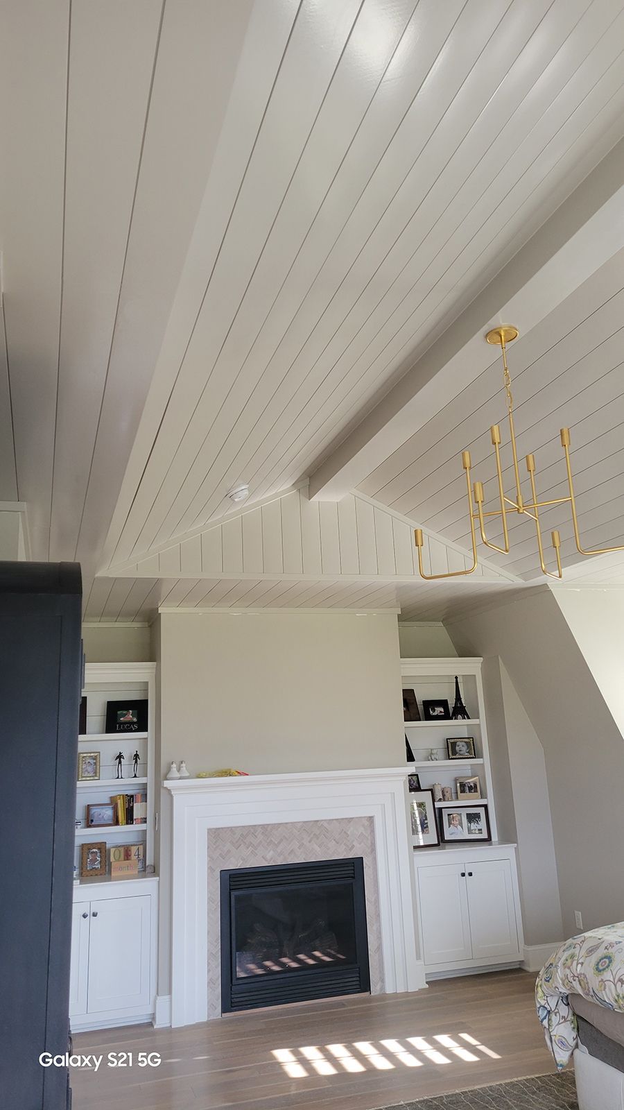 White paneled ceiling over a fireplace with built-in bookshelves. A gold chandelier hangs to the side.