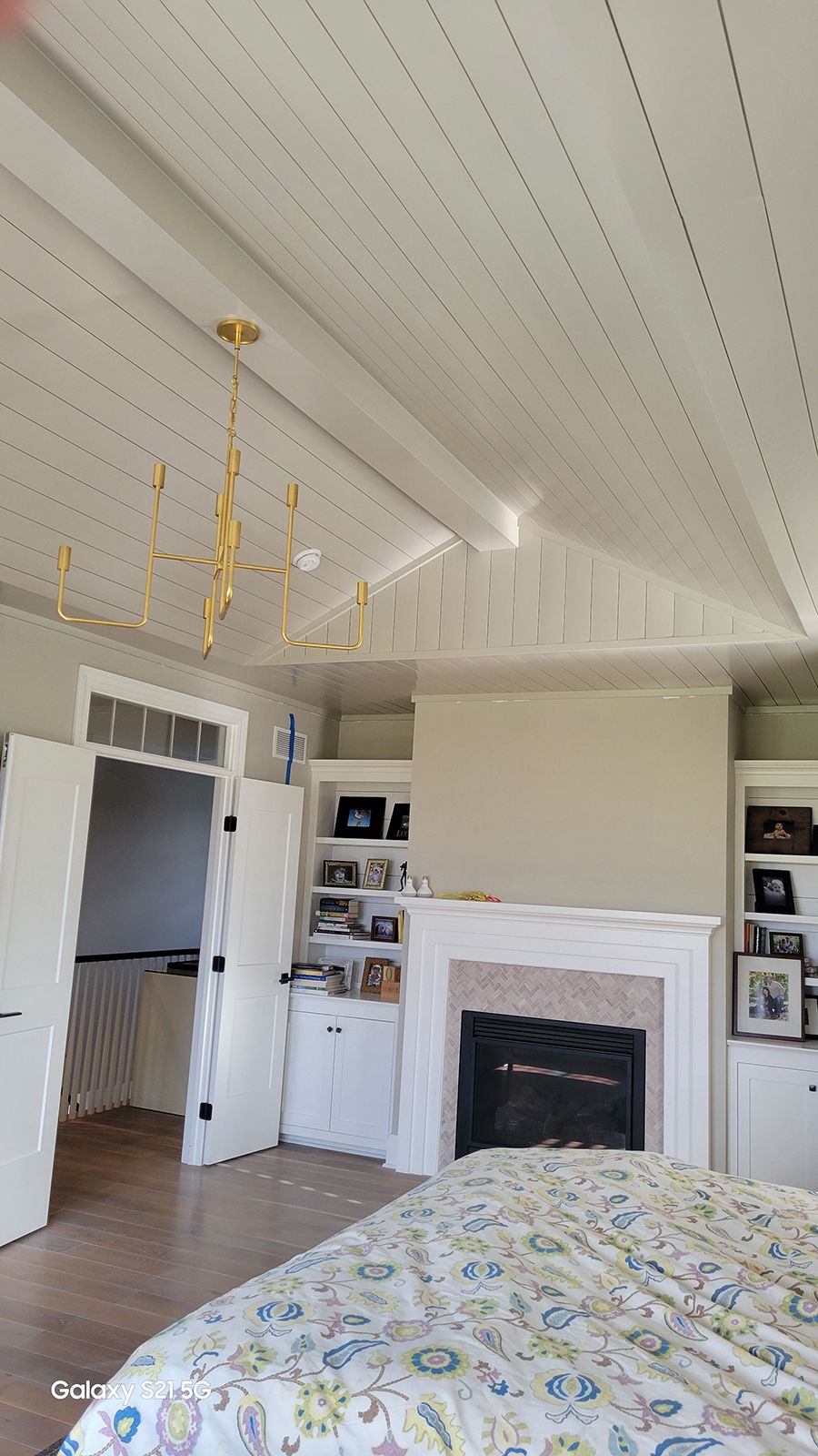 Bedroom with chandelier, fireplace, built-ins, and a bed with a floral patterned comforter.
