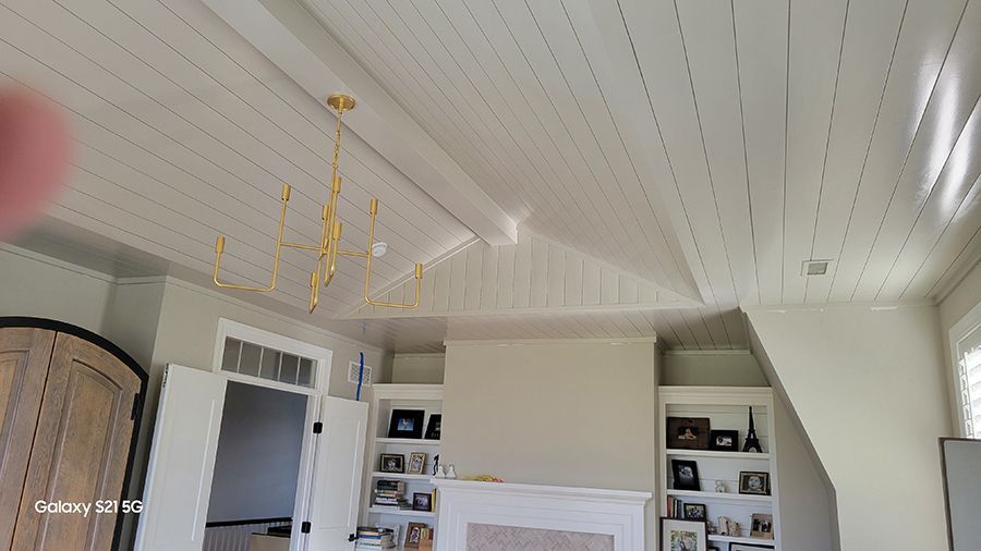 White-painted slatted ceiling with a gold chandelier. Built-in shelves flank a fireplace.